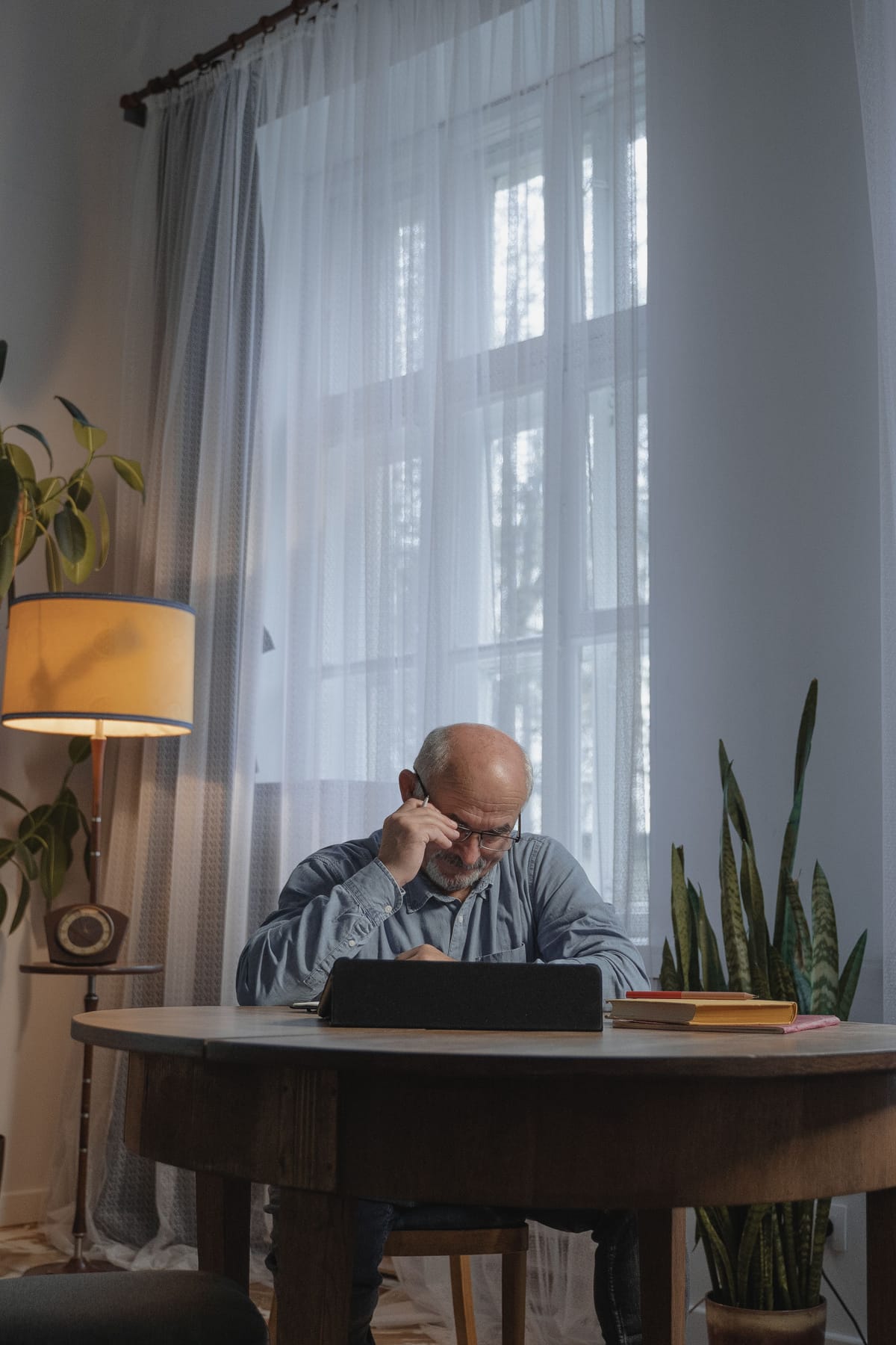 A silver-haired funeral director reading at a lamplit table in the evening.
